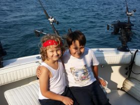 Two smiling kids enjoy a fun day on a fishing boat, capturing the joy of youth and adventure on the water.