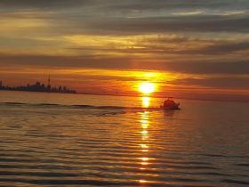 A serene sunset view over the water with a boat cruising past the Toronto skyline, creating a picturesque scene perfect for evening outings.