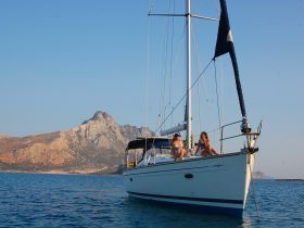 Two women enjoy a sunny day on a sailboat, surrounded by stunning mountain scenery — a perfect setting for sailing adventures.