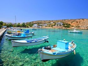 A picturesque view of colorful boats docked in crystal-clear waters, set against a scenic backdrop of hills and white buildings, perfect for capturing the charm of coastal life.