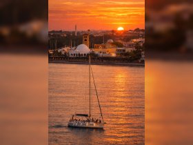 A sailboat glides through shimmering waters at sunset, with a group enjoying the scenic view — an ideal setting for memorable sailing experiences.