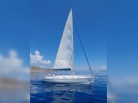 A beautiful sailboat glides through calm waters with crew members on deck, showcasing the perfect sailing experience under a clear blue sky.