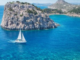 A picturesque aerial view of a sailboat navigating through crystal-clear waters near a rocky coastline, perfect for showcasing sailing adventures in stunning natural settings.