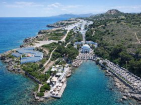 A stunning aerial view of a picturesque coastline featuring a beach area with umbrellas and people enjoying the clear turquoise waters, perfect for a relaxing getaway.