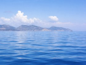 A serene view of the ocean with distant mountains under a clear blue sky, perfect for showcasing the beauty of coastal destinations.