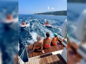A family enjoys a sunny day on the water, relaxing on the deck of a boat while paddleboarding nearby — perfect for summer adventures and family bonding.