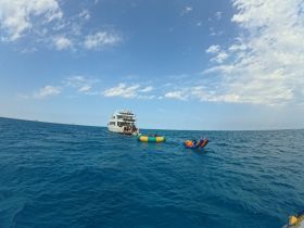A vibrant scene of guests enjoying on-water activities near a boat, featuring a floating mat and a thrilling inflatable ride — perfect for adventurous outings.