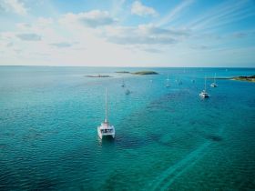 A stunning aerial view of a catamaran sailing in crystal-clear turquoise waters, surrounded by other boats and a picturesque island in the background, perfect for showcasing the beauty of sailing adventures.