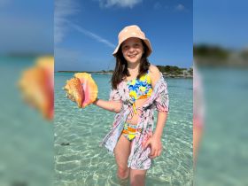 A young girl joyfully holds a colorful shell while wading in shallow waters, showcasing a delightful moment of exploration in a tropical paradise.
