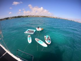 A vibrant scene featuring paddleboards, a floating mat, and a jet ski in clear turquoise waters, perfect for water sports and relaxation.