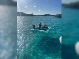 A group of friends relaxes on a floating mat in crystal-clear waters, enjoying a perfect day of sunbathing and fun in the Bahamas.