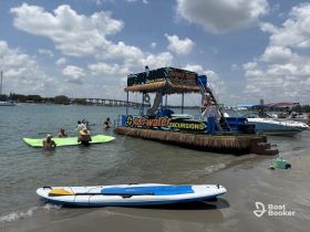A lively group enjoys a beach day with swimming and paddleboarding near a charter boat offering private excursions — perfect for family fun in the sun.