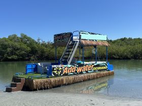 A vibrant tiki boat named 'Add-water Excursions' docked in calm waters, perfect for private trips and exploring scenic mangroves.