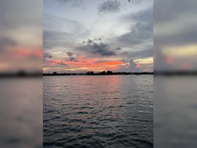 A stunning sunset over calm waters, showcasing vibrant colors and serene clouds — perfect for capturing the beauty of nature during a boating trip.
