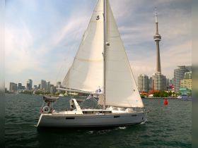 A sleek sailboat glides through the waters of Toronto, with the iconic CN Tower and city skyline in the background, showcasing a perfect day for sailing.