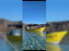 A vibrant yellow boat named 'Hija Tielson II' docked in clear waters, surrounded by scenic mountains — perfect for exploring coastal destinations.