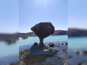 A stunning view of a unique rock formation with a boat in the background, showcasing the beautiful coastline and clear waters — perfect for exploring natural landmarks.