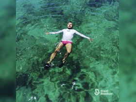A man floats peacefully in the crystal-clear waters, enjoying a moment of relaxation under the sun — a perfect scene for water lovers.