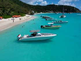 A vibrant scene of multiple boats anchored near a beautiful beach, with people enjoying the turquoise waters — perfect for a day of relaxation and fun in the sun.