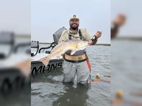 A proud angler holds up a freshly caught redfish while standing in shallow water, showcasing the thrill of fishing adventures on the water.