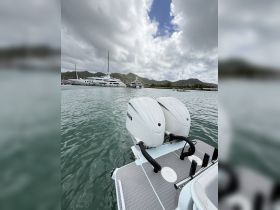A close-up view of outboard motors on a boat, with a marina backdrop featuring luxury yachts and lush mountains, showcasing the perfect setting for boating adventures.