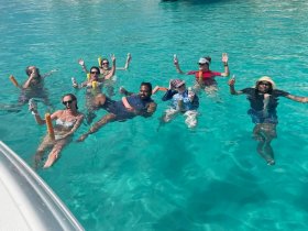 A lively group enjoys a fun day in the crystal-clear waters, celebrating with drinks and laughter — the perfect sandbar stop experience.