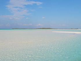 A stunning view of a serene beach with turquoise waters and a distant island, perfect for showcasing the natural beauty of tropical destinations.