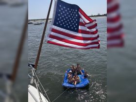 A lively group enjoys a fun day on a floating mat in the water, celebrating with drinks under the sun — perfect for summer outings and beach parties.