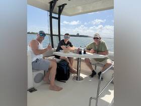 Three friends enjoy a relaxing moment inside a boat's cabin, sharing snacks and drinks while taking in the scenic waterfront views.