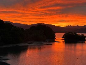A breathtaking sunset over a tranquil bay, with vibrant orange hues reflecting on the water — a perfect backdrop for evening boat adventures.