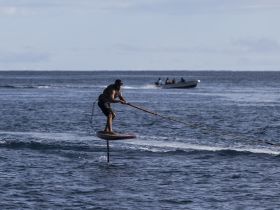 A thrilling moment captured as a rider foils above the water, showcasing the excitement of water sports. A boat can be seen in the background, adding to the dynamic scene.