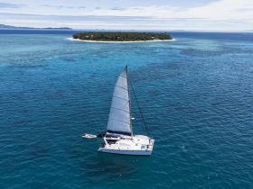 A stunning aerial view of a catamaran sailing through crystal-clear waters, with a picturesque island in the background, perfect for showcasing the beauty of sailing adventures.