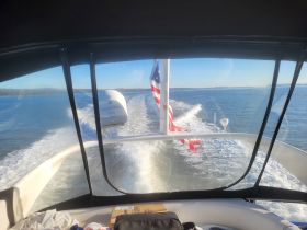 A view from the helm of a boat cruising through calm waters, showcasing the American flag and the boat's wake in the background — perfect for showcasing boating adventures.