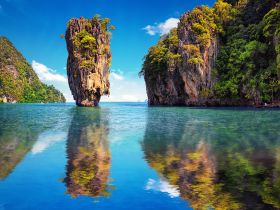 A stunning view of a towering rock formation surrounded by lush greenery and tranquil waters, reflecting the vibrant colors of the landscape — a perfect destination for nature lovers and boat tours.