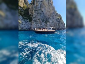 A lively group enjoys a scenic boat ride along stunning cliffs, showcasing the beauty of the coastline and vibrant blue waters.