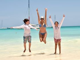 A joyful moment captured as a woman and two children jump in the shallow waters of a beautiful beach, showcasing family fun and adventure under the sun.