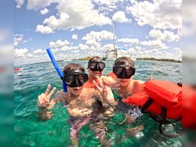A family enjoys snorkeling in clear waters, showcasing a fun day on the water with a boat in the background — perfect for aquatic adventures.