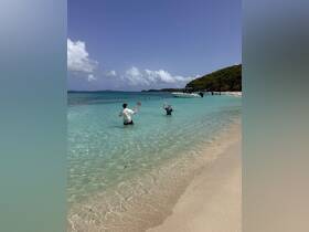Two friends enjoy a playful day at the beach, tossing a ball in the shallow waters while a boat is anchored nearby, capturing the essence of fun and relaxation on a sunny day.