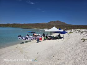 A lively scene at the beach with a fishing boat and a group enjoying their day under tents — perfect for a fun day of sportfishing and relaxation.