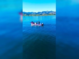 A group of friends enjoys a day on the water in a colorful boat, surrounded by stunning mountain scenery — perfect for outdoor adventures and lake excursions.