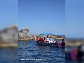 A lively group enjoys a boat tour near a striking rock formation, showcasing the beauty of the ocean and adventure on the water.