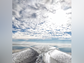 A serene view of the water's surface reflecting the sky, showcasing beautiful cloud formations and the wake of a boat — a perfect representation of tranquil boating experiences.