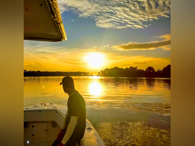 A serene sunset view from a boat, with a person enjoying the tranquil waters and vibrant colors reflecting on the surface — an ideal moment for relaxation and appreciation of nature.