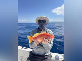 A proud angler holds up a vibrant fish against the backdrop of the open ocean, showcasing the thrill of a successful fishing trip.
