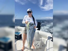 A woman proudly displays her impressive catch while fishing on a boat, showcasing the thrill of deep-sea fishing adventures.