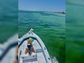 A woman relaxes on the bow of a boat, soaking up the sun while surrounded by vibrant turquoise waters — a perfect scene for a day of leisure on the water.
