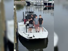 A group of three, including two minors, poses on a fishing boat at the dock, ready for a day of adventure on the water.