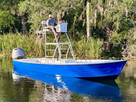 A man navigates a vibrant blue boat through serene waters, showcasing the perfect setting for fishing or leisurely outings in nature.