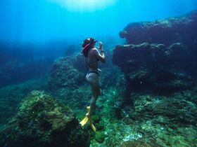 A snorkeler explores vibrant underwater rock formations, showcasing the beauty of marine life and adventure beneath the waves.