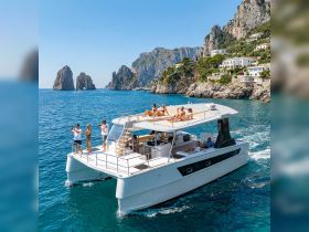 A lively group enjoys a sun-soaked day on a catamaran, capturing memories against the stunning backdrop of rocky cliffs and clear blue waters.
